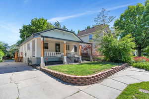 Shotgun-style home with a front lawn, covered porch, brick siding, and concrete driveway