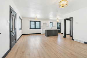 Kitchen with a chandelier, white cabinetry, a kitchen island, light countertops, and light wood-style flooring