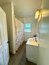 Bathroom with vanity, wood finished floors, toilet, baseboards, and a shower with curtain