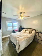 Carpeted master bedroom with ceiling fan, baseboards, and a textured ceiling