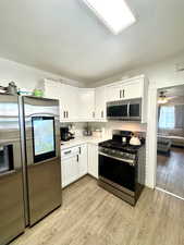 Kitchen with appliances with stainless steel finishes, white cabinets, light wood finished floors, tasteful backsplash, and light countertops