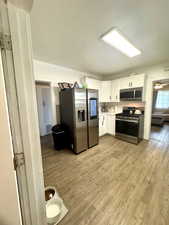 Kitchen with appliances with stainless steel finishes, light wood-style flooring, white cabinets, and light countertops
