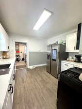 Kitchen with black range with gas cooktop, white cabinets, light countertops, light wood-style floors, and tasteful backsplash