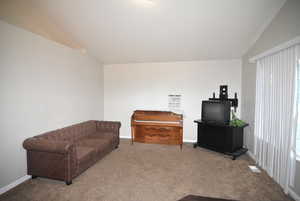 Living room featuring carpet flooring, baseboards, and lofted ceiling