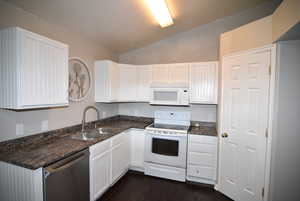 Kitchen with white appliances, a sink, lofted ceiling, white cabinets, and dark countertops