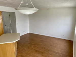 Unfurnished dining area with dark wood-type flooring, baseboards, and a textured ceiling