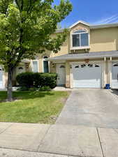 View of property featuring stucco siding, an attached garage, a front lawn, and concrete driveway