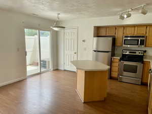 Kitchen featuring appliances with stainless steel finishes, light countertops, hardwood / wood-style floors, pendant lighting, and a textured ceiling