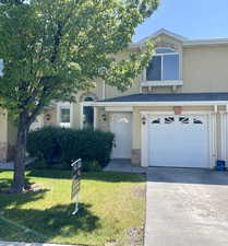 Multi unit property featuring an attached garage, a front lawn, stucco siding, and concrete driveway
