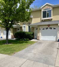 View of front of home featuring a garage, stucco siding, a front yard, driveway, and stone siding