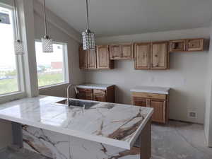Kitchen featuring a sink, lofted ceiling, light countertops, and hanging light fixtures