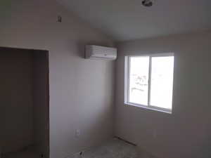 Empty room featuring an AC wall unit, plenty of natural light, and vaulted ceiling