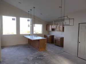 Kitchen with vaulted ceiling, a sink, concrete floors, brown cabinetry, and a peninsula