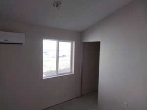 Unfurnished room featuring a wall mounted AC and vaulted ceiling