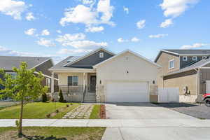 View of front of home with stucco siding, driveway, an attached garage, a porch, and stone siding
