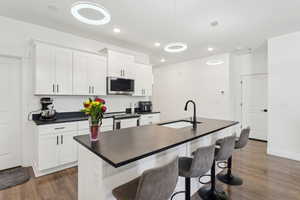 Kitchen with a sink, dark countertops, stainless steel appliances, dark wood-style flooring, and an island with sink