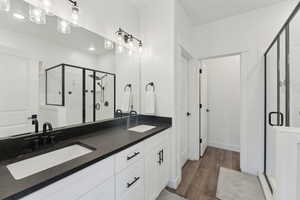 Full bath featuring a shower stall, double vanity, wood finished floors, and baseboards