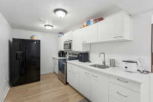 Kitchen featuring appliances with stainless steel finishes, a sink, light wood-style flooring, white cabinets, and a textured ceiling