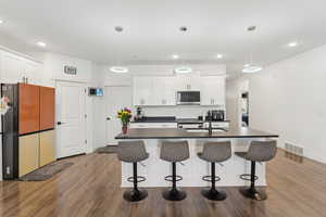 Kitchen with freestanding refrigerator, dark countertops, stainless steel microwave, wood finished floors, and white cabinetry