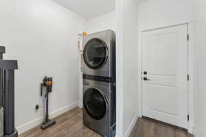 Laundry room with stacked washing machine and dryer, wood finished floors, and baseboards