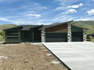 Mid-century inspired home featuring an attached garage, a mountain view, concrete driveway, stone siding, and a shingled roof