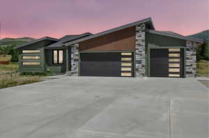 Contemporary home featuring stone siding, a garage, driveway, and a mountain view