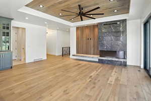 Unfurnished living room with a raised ceiling, wood ceiling, recessed lighting, light wood-style flooring, and a high end fireplace