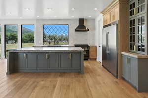 Kitchen with high end appliances, wall chimney range hood, a kitchen island, light wood-style floors, and backsplash