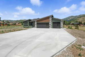 View of front of house featuring a mountain view, stone siding, a garage, and concrete driveway