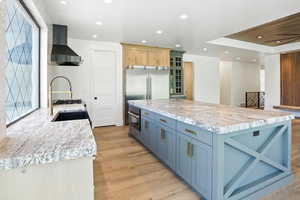 Kitchen featuring wall chimney exhaust hood, light wood-style flooring, recessed lighting, glass insert cabinets, and a kitchen island