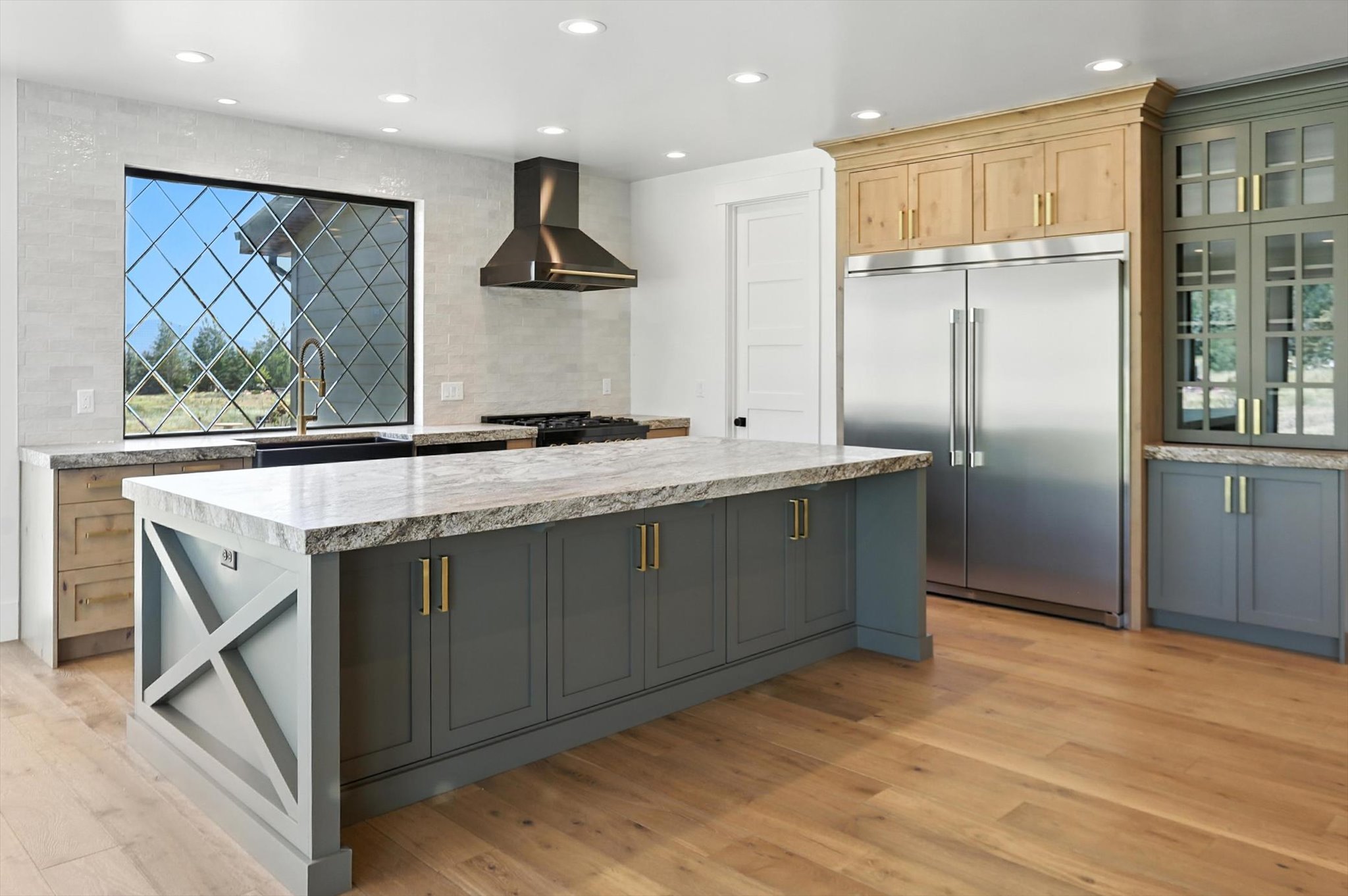 Kitchen featuring wall chimney exhaust hood, built in fridge, backsplash, light wood-style flooring, and a kitchen island