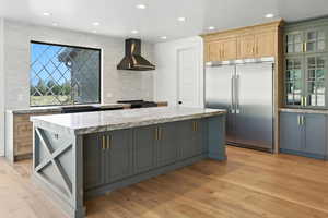 Kitchen featuring wall chimney exhaust hood, built in fridge, backsplash, light wood-style flooring, and a kitchen island