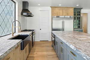 Kitchen featuring wall chimney exhaust hood, high end appliances, light wood-style flooring, recessed lighting, and light stone counters