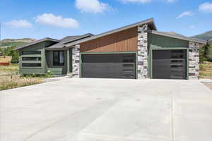 View of front facade featuring stone siding, a garage, board and batten siding, a mountain view, and concrete driveway