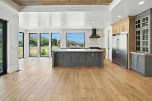 Kitchen with stainless steel built in refrigerator, wall chimney range hood, gray cabinets, light wood-style flooring, and recessed lighting