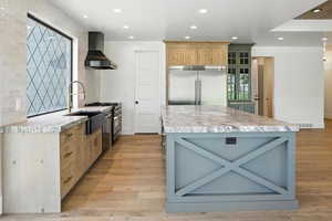 Kitchen with wall chimney range hood, premium appliances, light countertops, light wood-style flooring, and recessed lighting