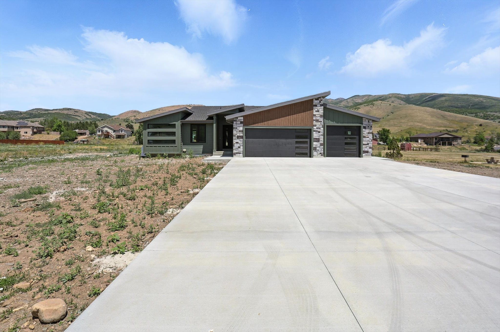 Modern home featuring a mountain view, a garage, stone siding, and driveway