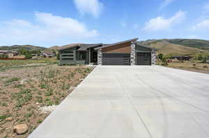 Modern home featuring a mountain view, a garage, stone siding, and driveway