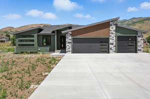 Mid-century modern home with a garage, a mountain view, stone siding, and driveway