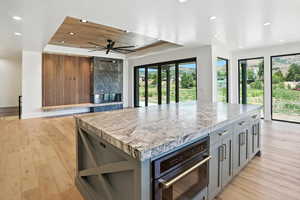 Kitchen featuring recessed lighting, gray cabinetry, a raised ceiling, a center island, and light wood-style flooring