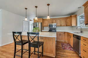 Kitchen with stainless steel appliances, a sink, light wood-style flooring, a center island, and a kitchen bar