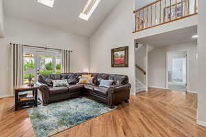 Living area with high vaulted ceiling, stairway, a skylight, light wood-type flooring, and baseboards