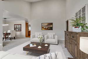 Living area featuring light carpet, baseboards, a towering ceiling, ornamental molding, and plenty of natural light