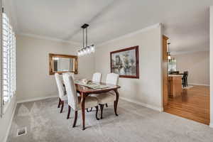 Dining room featuring light carpet, a chandelier, ornamental molding, and baseboards