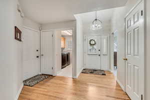 Entryway with washer / clothes dryer, a chandelier, light wood finished floors, and baseboards