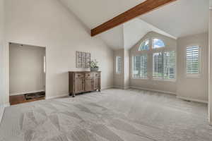 Empty room with light carpet, baseboards, high vaulted ceiling, and beam ceiling