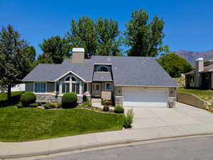View of front of house featuring stone siding, an attached garage, stucco siding, a chimney, and driveway