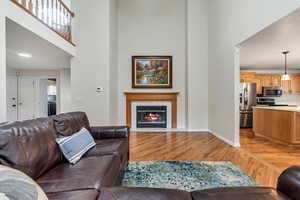 Living area with a high ceiling, light wood-type flooring, a tiled fireplace, and baseboards
