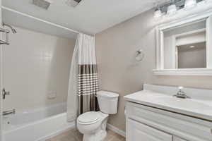 Full bathroom with vanity, tile patterned floors, toilet, shower / bath combination with curtain, and baseboards