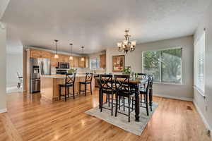 Dining room featuring healthy amount of natural light, light wood-style floors, a chandelier, and baseboards